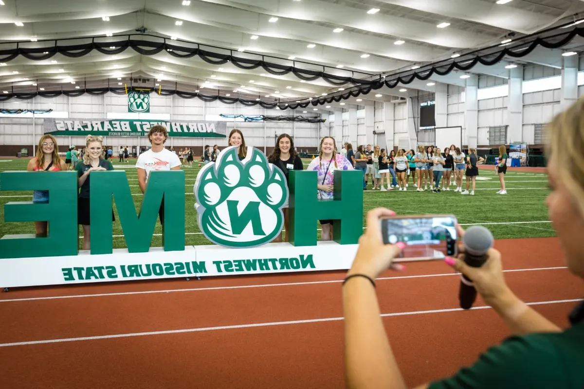 Students take a picture with the Northwest Home sign at the Hughes Fieldhouse, where the student services fair is held before the first SOAR session begins.